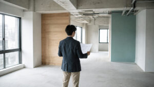 内装工事前の空きテナントで間取り図を手に室内を見渡す人物の後ろ姿