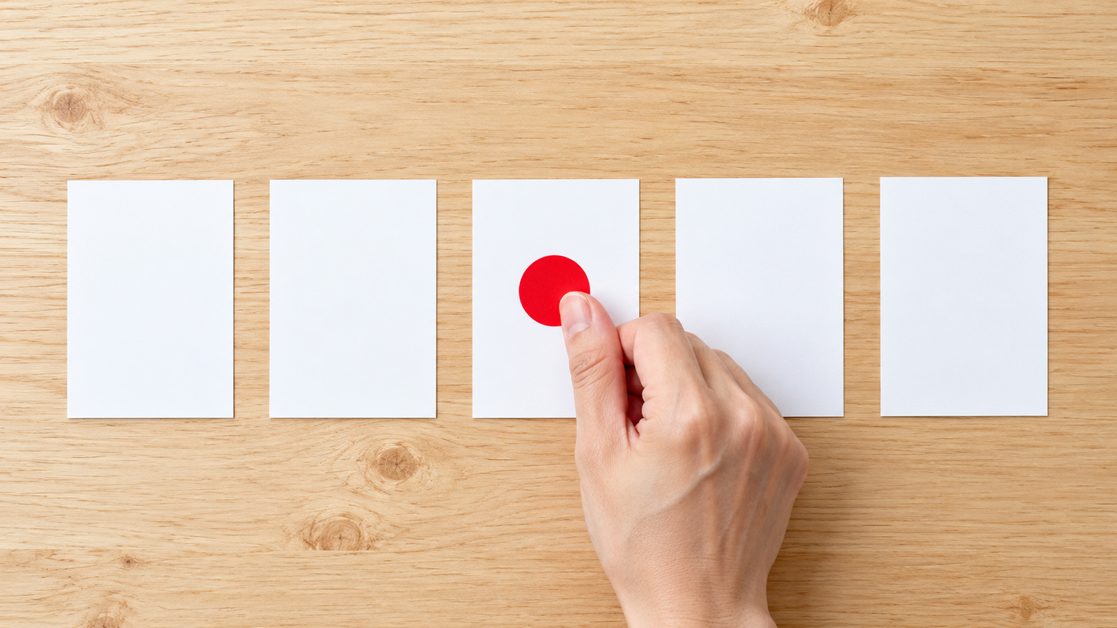 並んだ白いカードのうち1枚にだけ赤い丸シールを貼り、目印を付けるイメージ